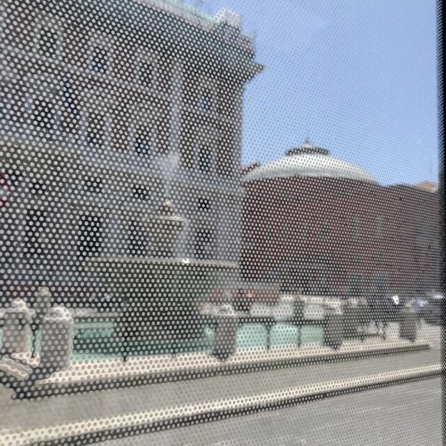 Vista da un vetro dell'autobus di corso cavour a Bari: un edificio dietro una fontana e in lontananza il teatro petruzzelli