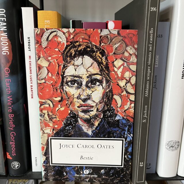 romanzo Bestie di Joyce Carol Oates fotografato in una libreria. In copertina un volto di donna rappresentato con la tecnica mosaico