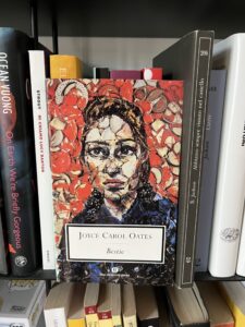 romanzo Bestie di Joyce Carol Oates fotografato in una libreria. In copertina un volto di donna rappresentato con la tecnica mosaico